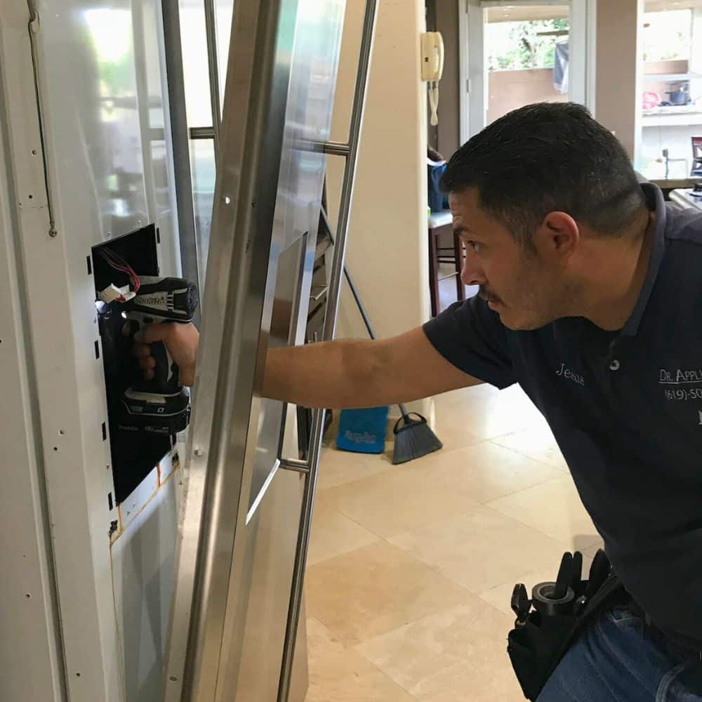 A technician works on an ice dispenser during a refrigerator installation.
